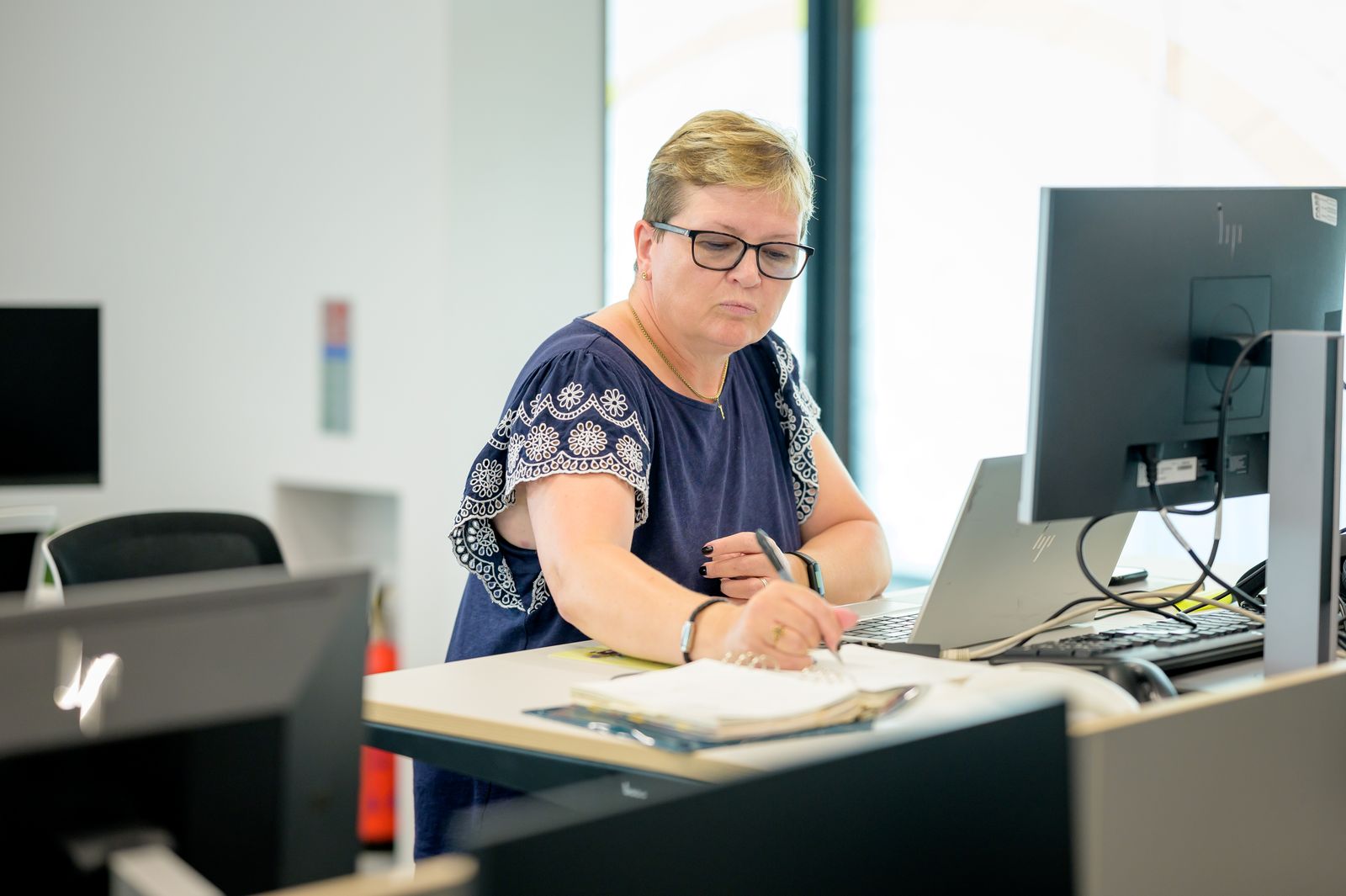 Woman writing in a notebook beside a laptop.